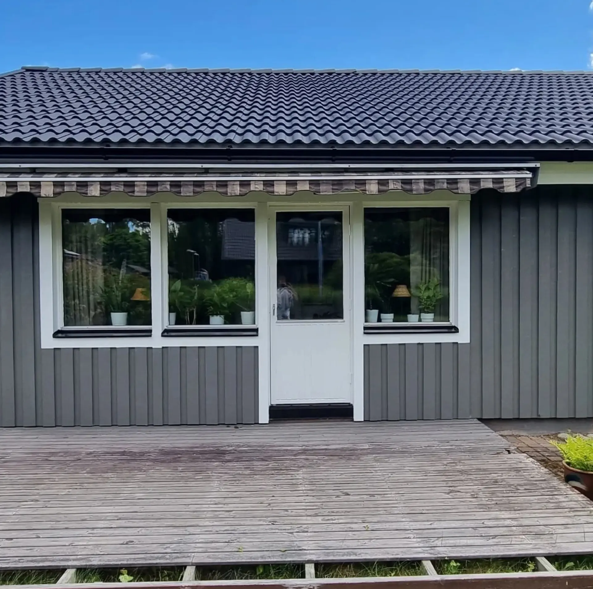 Färdigmålad mörkgrå verandafasad med vit dörr och vita foder.