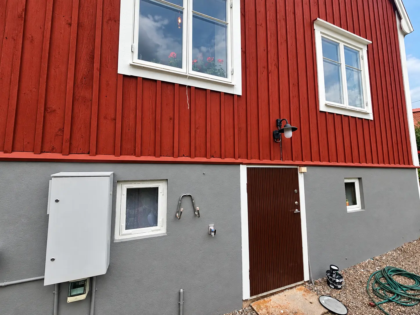 Röd träpanel och grå sockel med målarutrustning på marken.