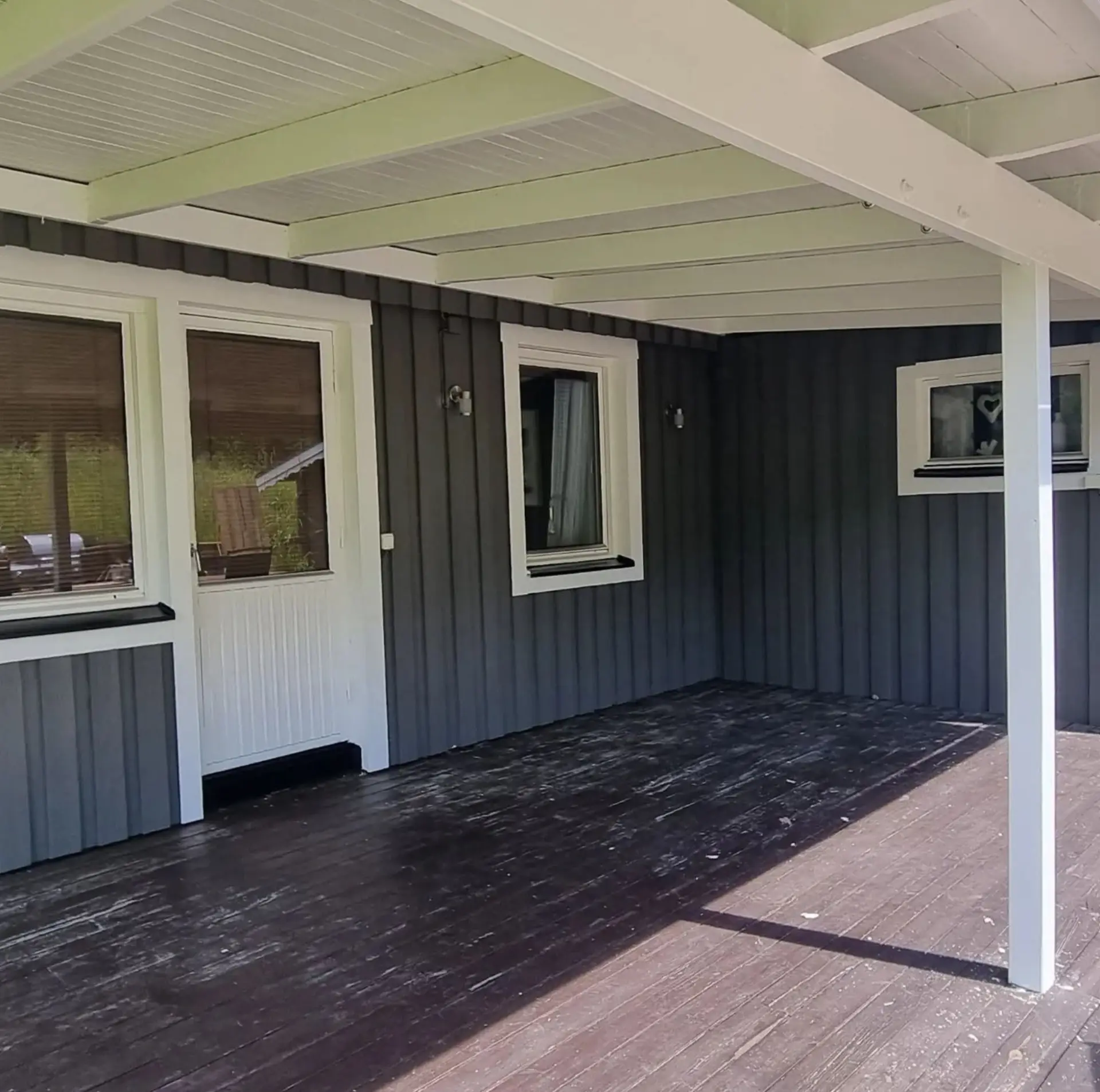 Färdigmålad mörkgrå fasad under verandatak med vita detaljer.