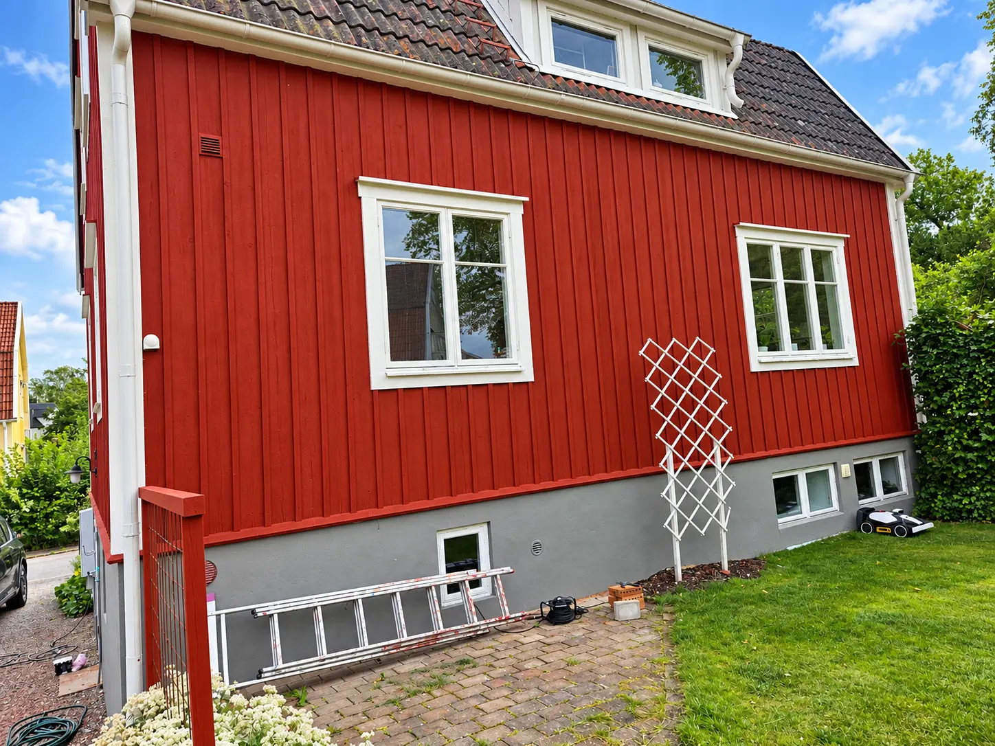 Rödmålad fasad med stege och spaljé framför väggen.