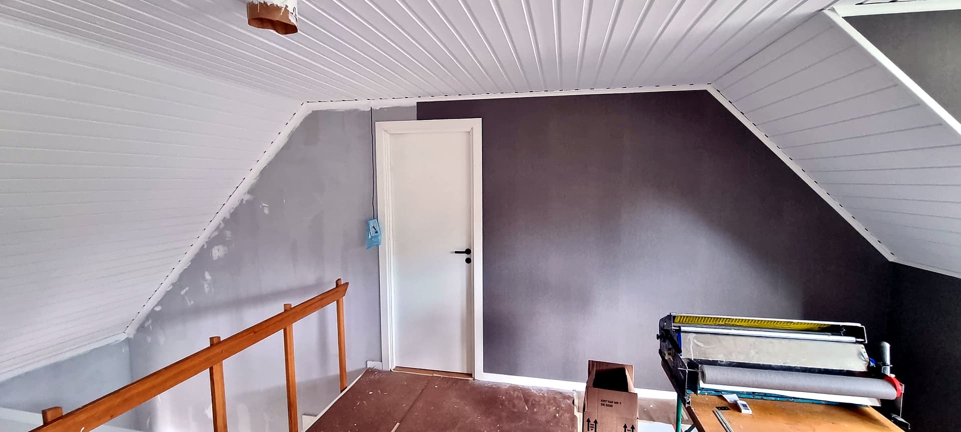 Vindsplan under tapetsering med grå tapet och vitt paneltak.