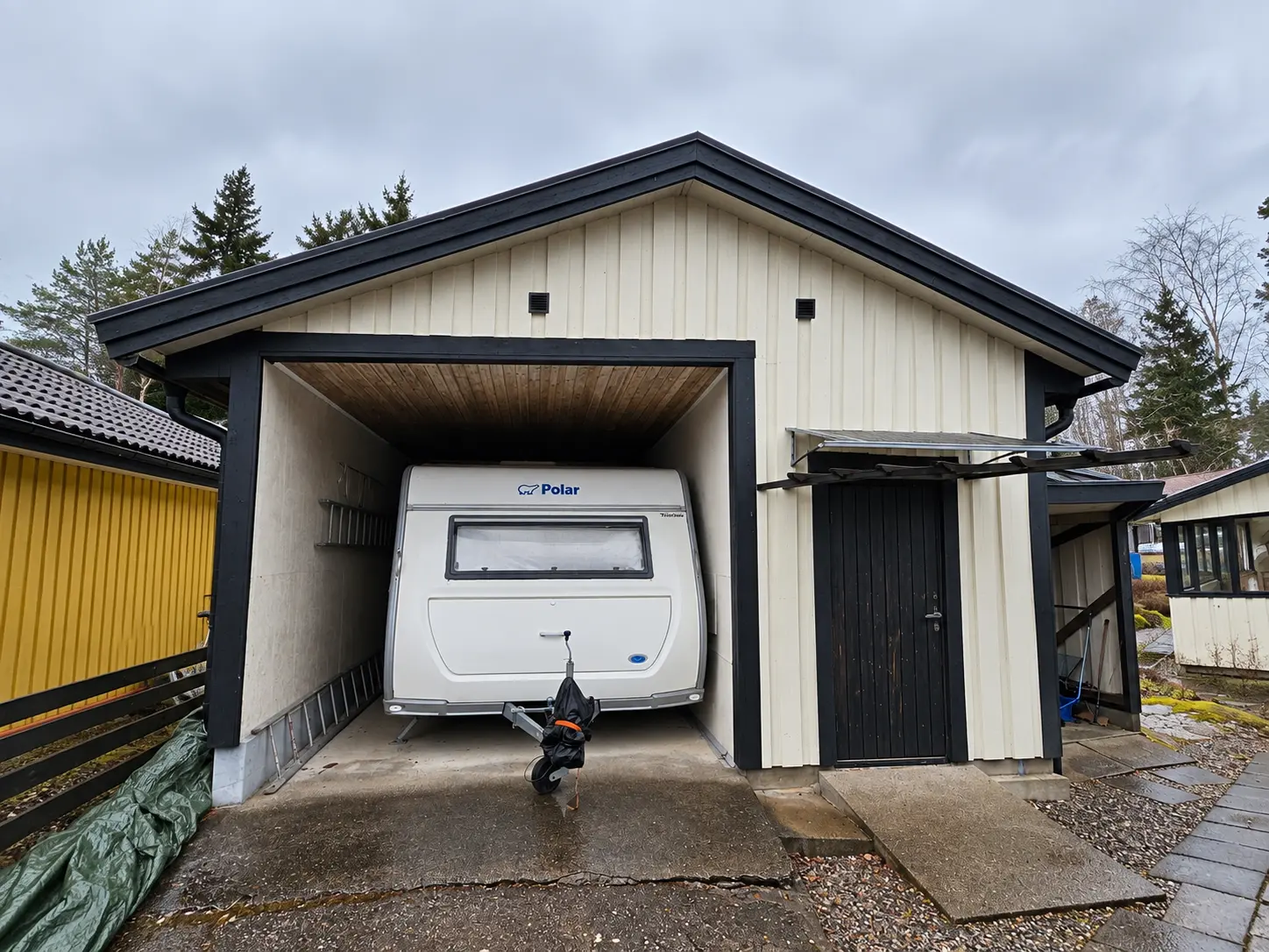 Krämvitt garage med svarta knutar och carport.