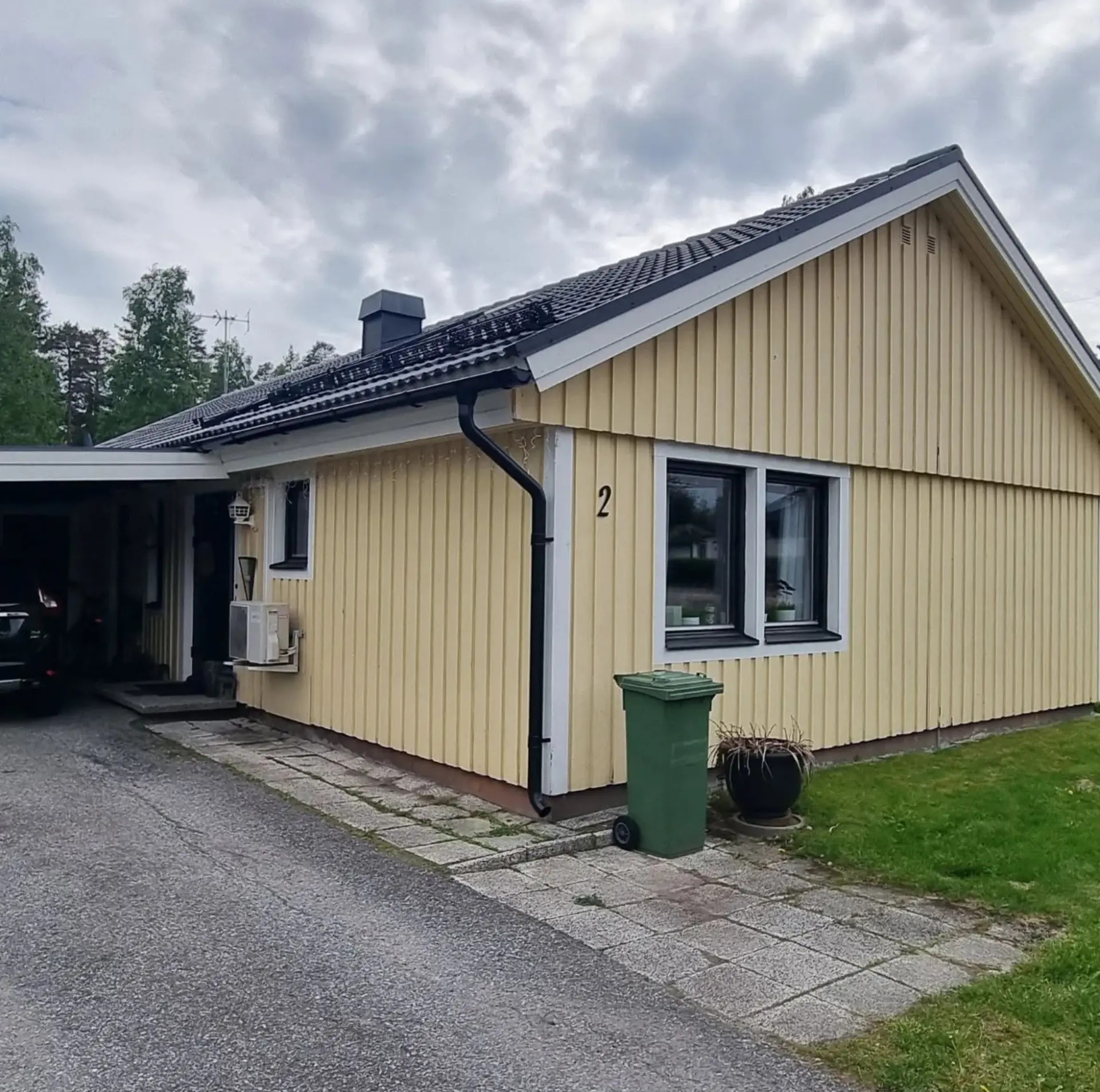 Ljusgul träfasad med gavel, fönster och carport före ommålning.