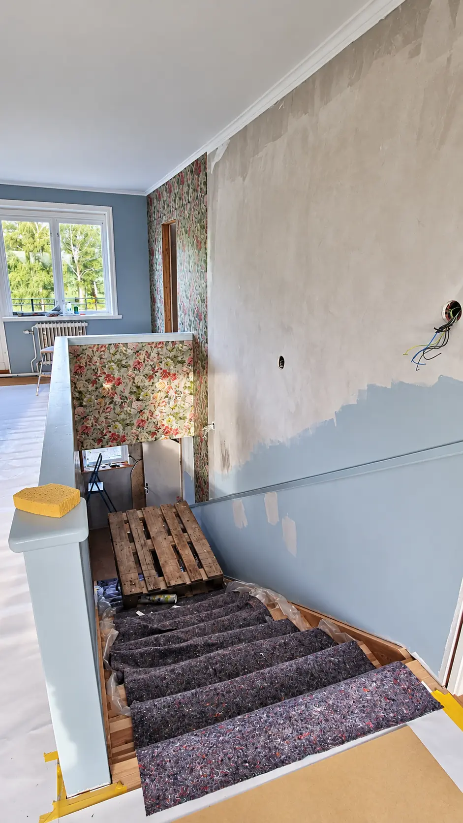 Vägg under spackling och målning, med trappa och skyddsfilt.