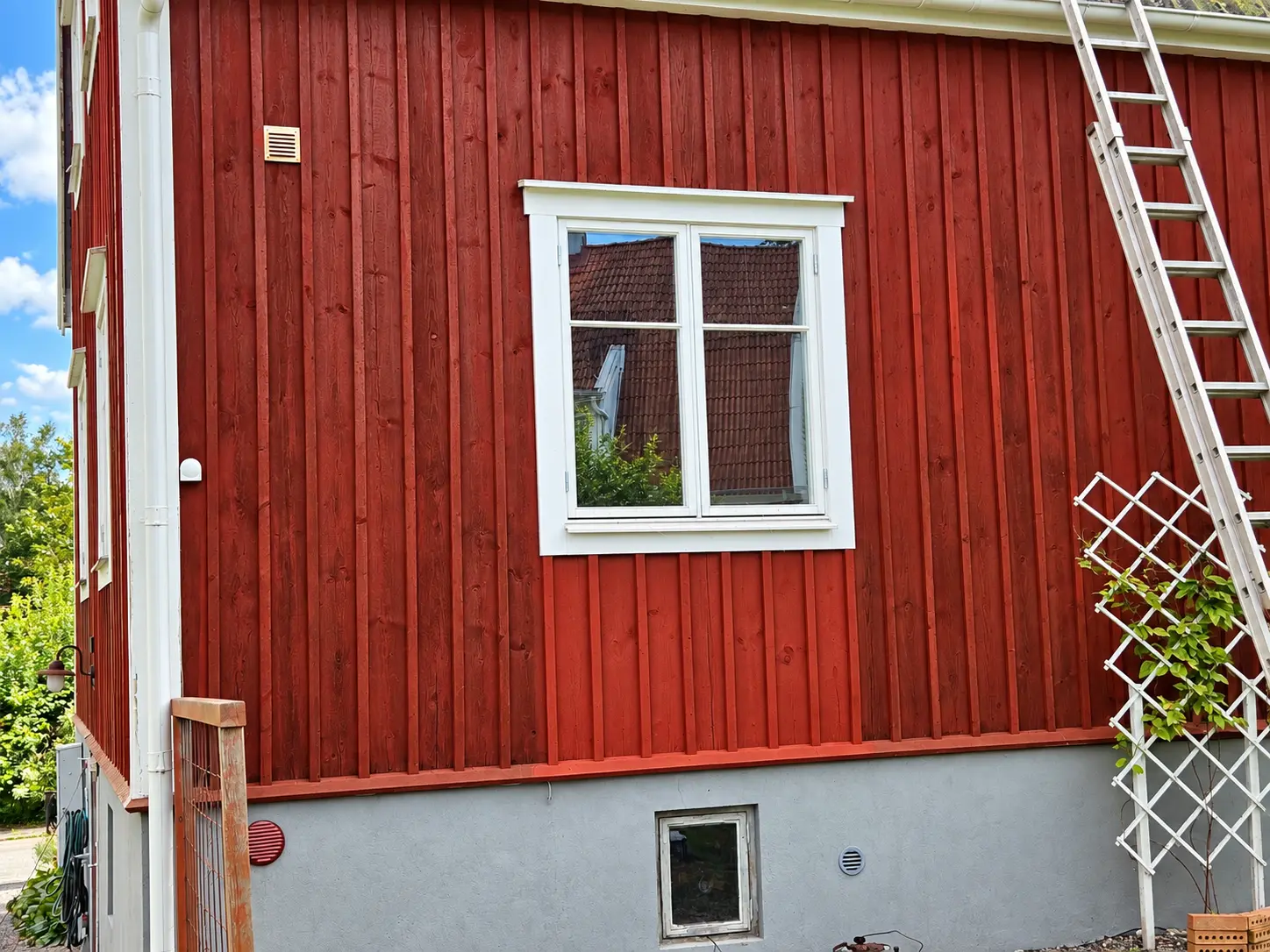 Fasad med provmålad yta under fönstret och stege lutad mot väggen.